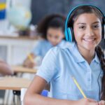 Lachend meisje met een koptelefoon tegen geluid in de klas, met een potlood in haar hand